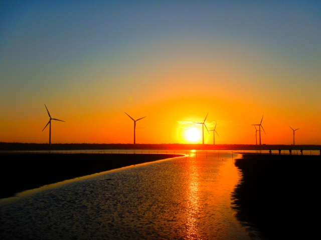 夕日と風力発電の風車が並ぶ水辺の美しい夕景